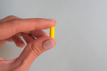 woman hand holding yellow pill capsule on light blue background, medication concept with copy space