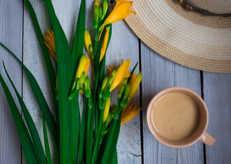 a bouquet of yellow lilies, a hat and a Cup of coffee on a wooden table, breakfastの写真素材