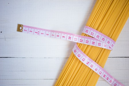 Measuring tape,diet theme. with bunch of uncooked Italian pasta spaghetti on the white wooden...