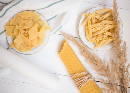 varieties of pasta on a white wooden table, spaghetti, Penne, maltagliati, local cuisineの写真素材