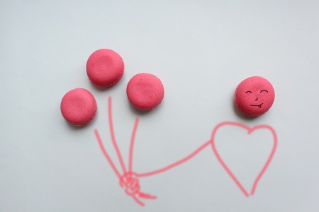 Three pink macaroons in the form of balloons in the hand of man on a blue background.の写真素材