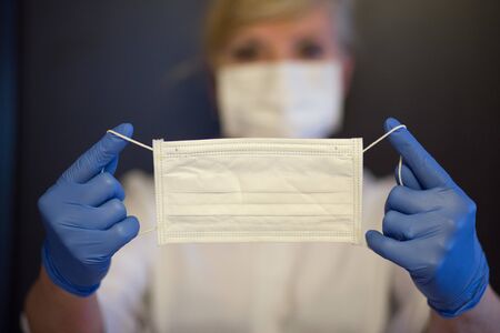 Senior woman wearing mask, gloves holds a a mask in hands. Selective focus. Coronavirus and epidemic virus symptoms.の写真素材