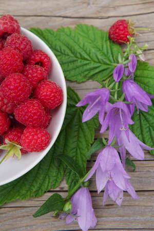 ripe raspberries with leaves and flowers on a wooden table.の写真素材