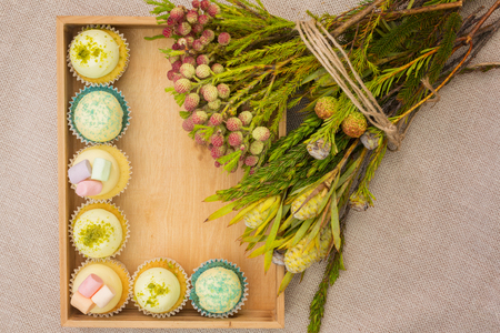 Different cupcakes in a wooden box with a posy of forest flowersの写真素材