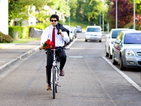 Businessman is riding a bicycle in a suit coming after work with bouquet of red rosesの写真素材