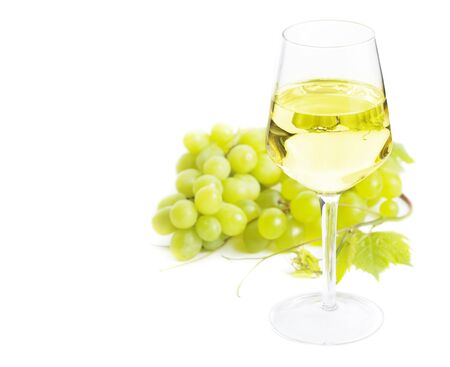 Glass of white wine with grapes and green leaves over white with copy spaceの写真素材