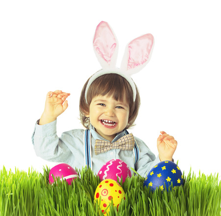 Laughing baby boy with bunny ears, bow tie, suspenders hunting for Easter eggs in a green grass....
