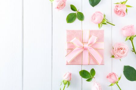 Spring pink flowers, green leaves and gift box on white wooden background. Flat lay, top view, copy space.の写真素材