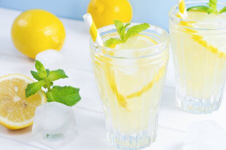Glasses with summer drink lemonade, lemon fruit and mint leaves on white wooden table.の写真素材