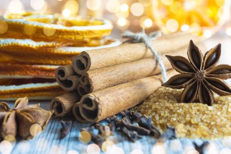 Christmas spices - cinnamon sticks, star anise, cloves and slices of dried orange on Christmas lights background.の写真素材