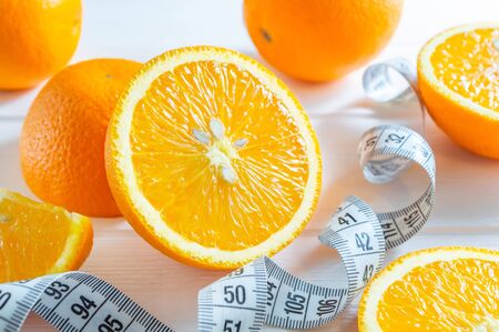 Fresh sliced and whole oranges, and measuring tape on white wooden table.の写真素材