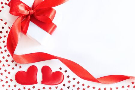 Gift or present box with red ribbon, decorative hearts and stars confetti on white background. Holiday concept, flat lay, top view.の写真素材