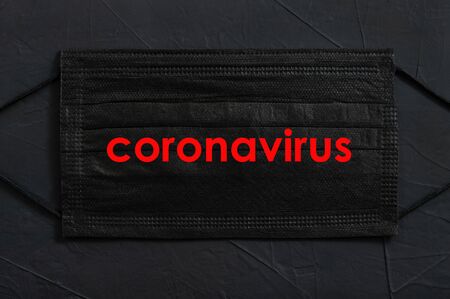 Coronavirus, nCoV-19, COVIN-19 concept. Black disposable protective mask with CORONAVIRUS text on black background.の写真素材