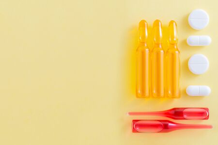 Yellow and red ampoules of vaccine and white pills on yellowの写真素材