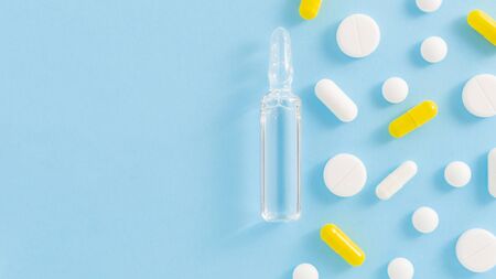 Transparent ampoule with vaccine and white and yellow pills on blue background. Top view with copy space.の写真素材