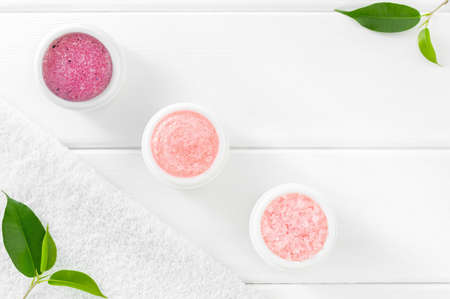 Rose cosmetic set for body care: scrub, exfoliant, sea salt and bath towel on white wooden background with green leaves.の写真素材