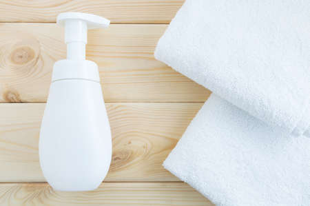 White bottle with dispenser and two white towels on a natural wooden background. Flat lay, top view.