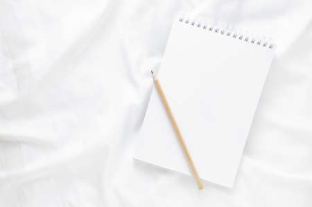 Notepad with copy space and pencil on white bed sheets. Concept of working from home or making plans in the morning.の写真素材