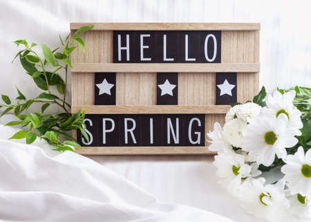 Hello Spring text on wooden board with white flowers and green leaves on white bed linen.の写真素材