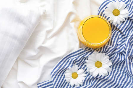 Orange juice and chamomile flowers on bed with white linens and blue bedspread.の写真素材