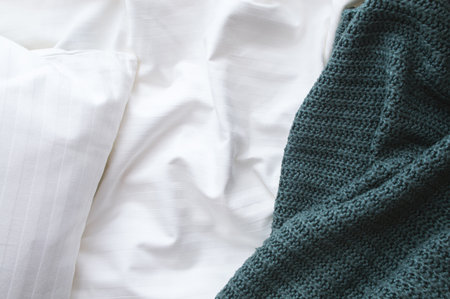 Top view of a unmade bed with rumpled sheet, knitted blanket, and pillow.の写真素材