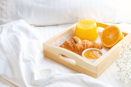 Continental breakfast in bed with growing, orange juice and jam on wooden tray.の写真素材