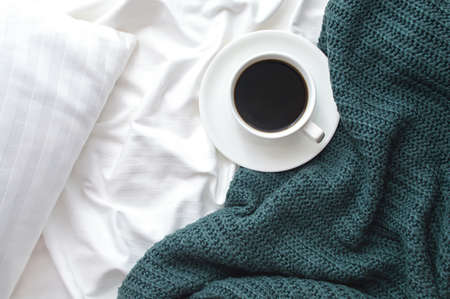 Cup of americano coffee on the bed with white linens and green bedspread. Morning coffee concept.の写真素材