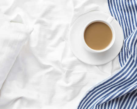 Cup of coffee with milk on the bed with white linens and blue bedspread. Morning coffee concept.の写真素材