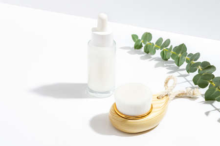 Cosmetic facial serum, washing brush and eucalyptus leaves on white background. Natural cosmetics and spa concept.の写真素材