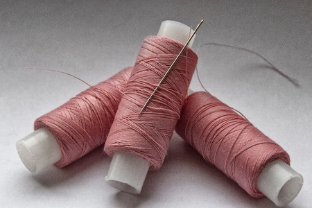spool of pink thread with a needle on white backgroundの写真素材