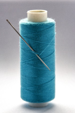 spool of blue thread with a needle on white backgroundの写真素材
