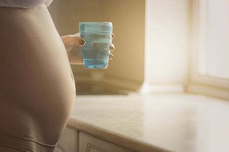 Good looking pregnant woman holding a glass of water while standing in the kitchenの写真素材