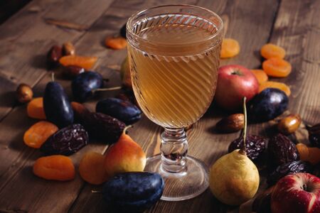 A glass cup with apricot apple plum pear fruit compote and ripe apricots on a wooden table. Sweet and healthy dessert.の写真素材