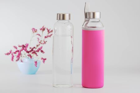 Two clear glass bottles one in a pink case with clean waterの写真素材