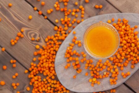 sea buckthorn of the morse in a beautiful glass on a wooden background of berries scatteredの写真素材