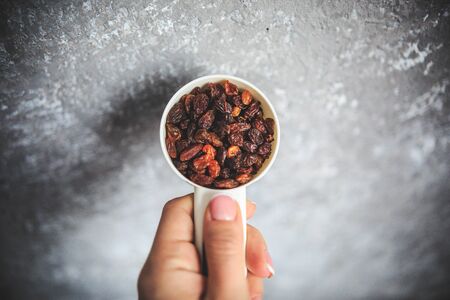 Raisins in the white measuring cup taken from the top on the gray and white background holding in hand.の写真素材