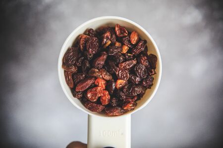 Raisins in the white measuring cup taken from the top on the gray and white background.の写真素材