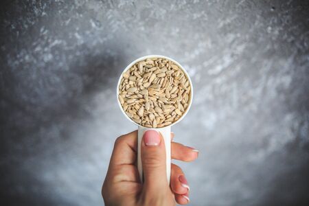 Natural sunflower seeds without shell in the white measuring cup taken from the top on the gray and white background.の写真素材