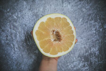 Tropical summery fruit called Pommelo looking fresh and juicy holding in hand on the gray and white...