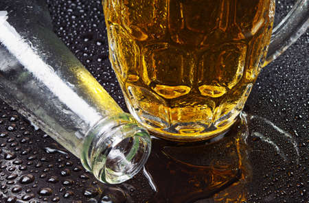 Glass of beer and an empty bottle with drops of waterの写真素材