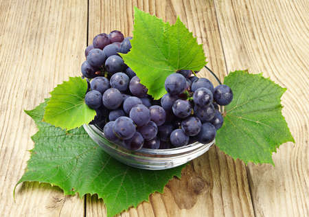 Ripe grapes with leaves in a glass cup on wooden backgroundの写真素材