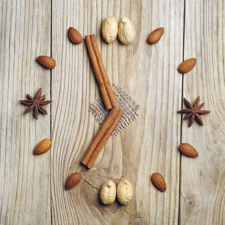 Cinnamon sticks, star anise and nuts in the form of clock on wooden tableの写真素材