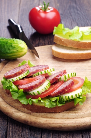 Sandwiches with sausage, lettuce, tomato and cucumber on a cutting boardの写真素材