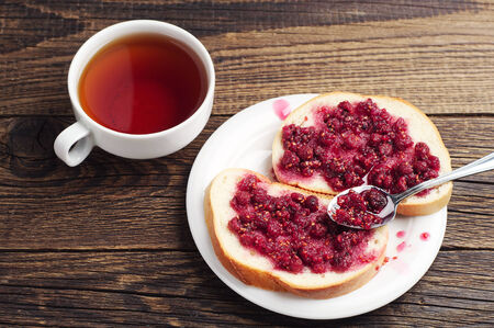 White bread with raspberry jam and cup of tea on tableの写真素材