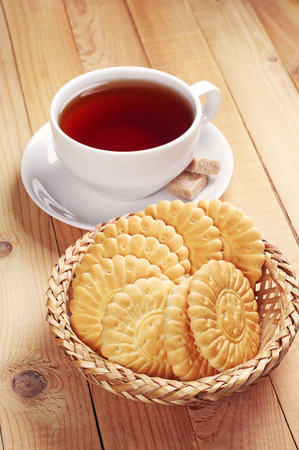 Cookies in wicker bowl and cup of tea on wooden tableの写真素材
