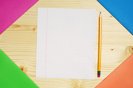 Multicolored exercise books and a single clean sheet on table 