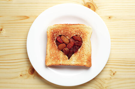 Slice of bread with cut out heart shape and raisins on wooden tableの写真素材