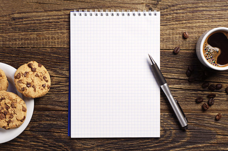 Opened notepad and cup of coffee with chocolate cookies on vintage wooden table. Top viewの写真素材