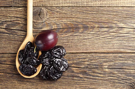 Prunes with plums in spoon and near on vintage wooden background. Top viewの写真素材