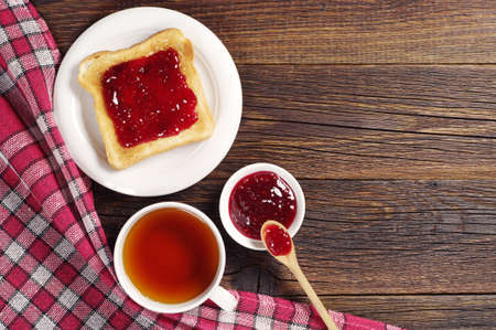 Cup of tea and toast with raspberry jam on old wooden table. Top view